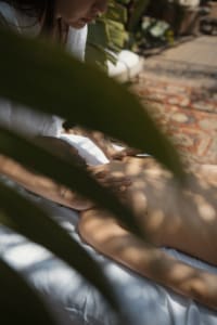 Trattamento benessere all’aperto presso The Sanctuary Roma: una persona riceve un massaggio rilassante immersa nella natura, tra luci e ombre create dalle foglie tropicali. Un’esperienza sensoriale in cui mente, corpo e anima si rigenerano per raggiungere il proprio massimo equilibrio interiore.